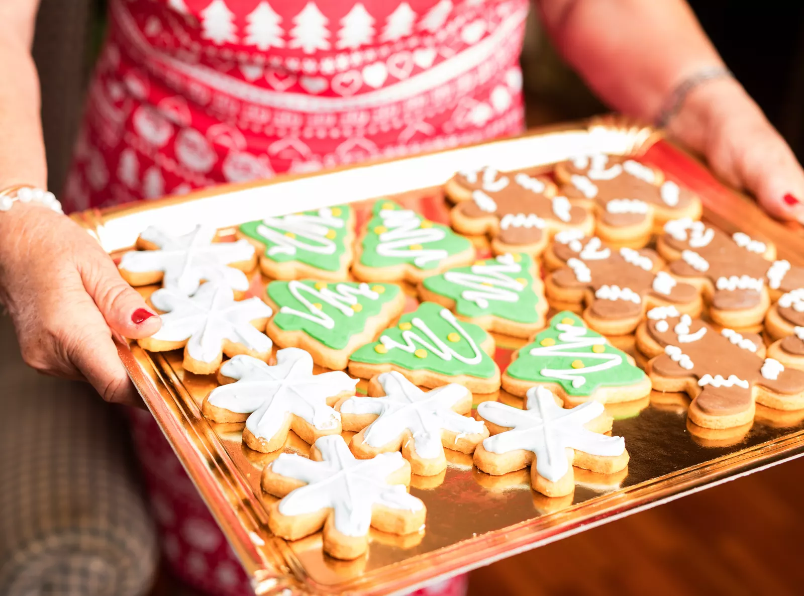 Family carrying a tray of fresh-baked Christmas cookies in a warmly lit kitchen