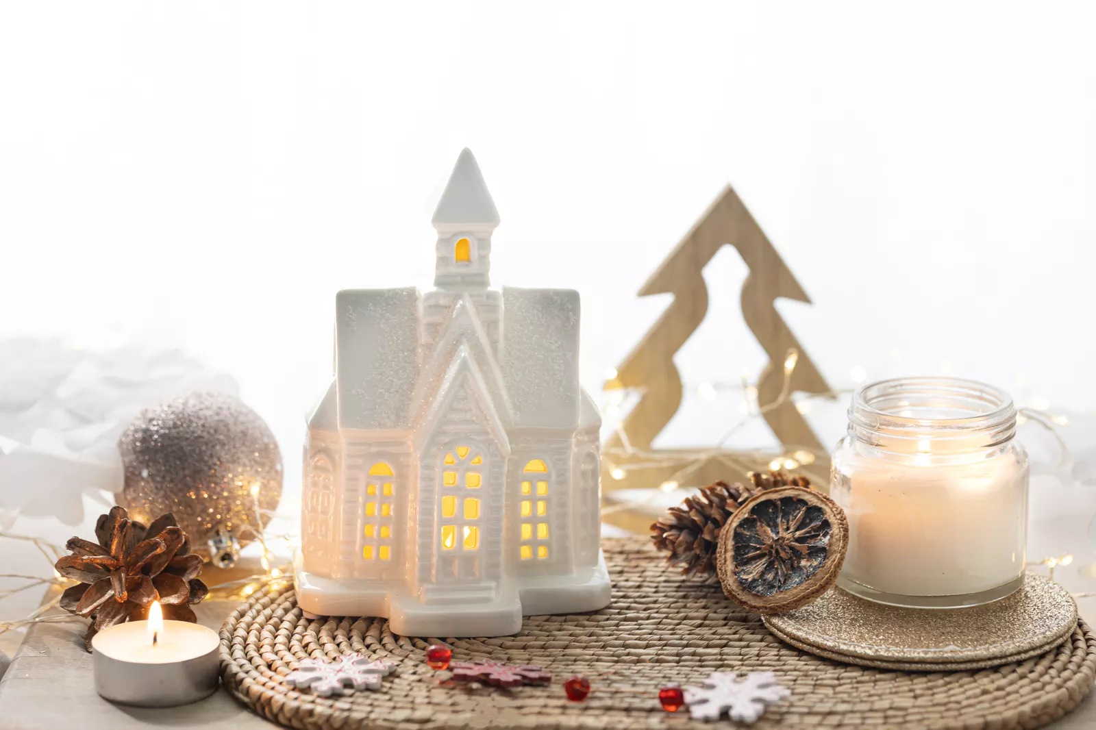 Christmas still life of glowing string lights, ornaments, and a little decorative house