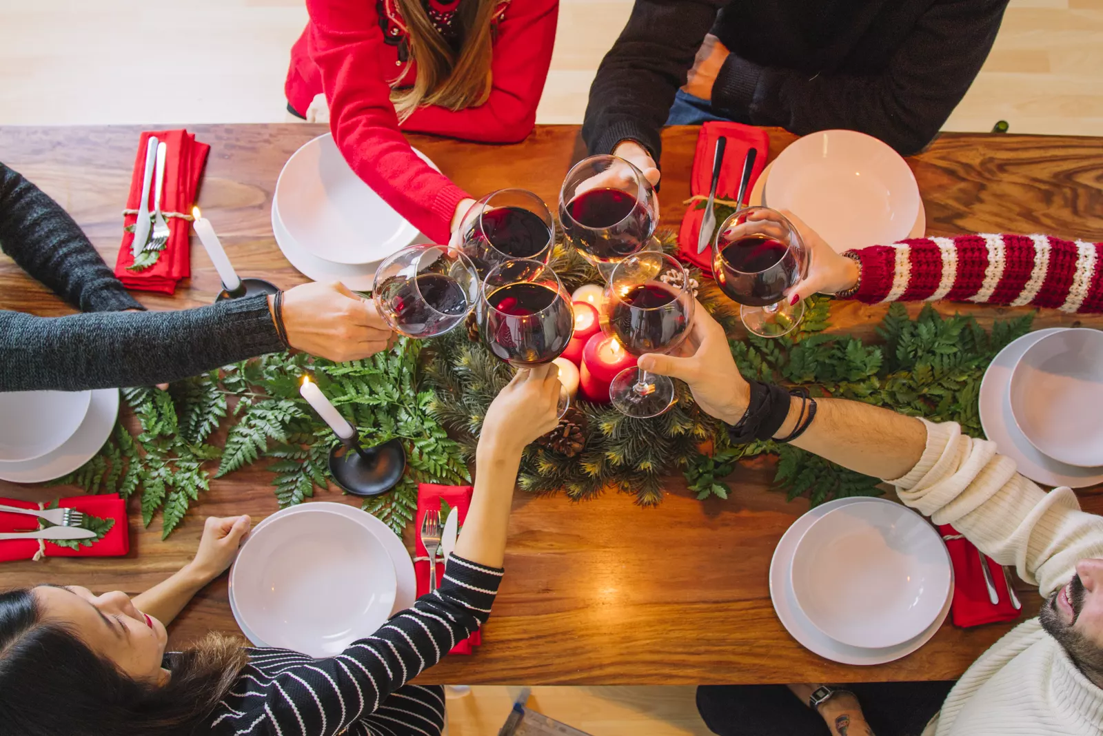 Candlelit Christmas dinner table set with wine, evergreen sprigs, and festive dishes